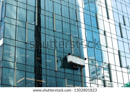 Workers crane cradle clean windows glass of high building under sun day light blur sky, Hoist washer cleaning platform elevator maintenance on skyscraper high-rise tower facade, copy space text logo