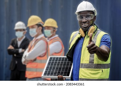 Workers Engineering Standing And Holding Solar Panel With Working Suite Dress And Safety Helmet. Group Men Worker Wearing Face Mask Standing In Front Container Wall Cargo.