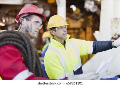 Workers Examining Blueprints On Oil Rig