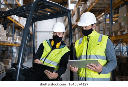 Workers with face mask and tablet working indoors in warehouse, coronavirus concept.
