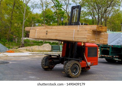 Workers in front of forklift stacker loader palette home framing beams for house under construction.