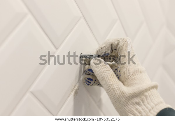 Worker\'s hand in glove inserts wall pvc dowel in\
wall cladded with tile\
ceramic