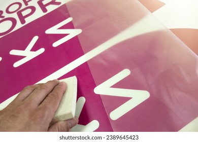 A worker's hand with a soft felt squeegee for vinyl film stickers. Decoration of shop windows with inscriptions. Advertising for the store.