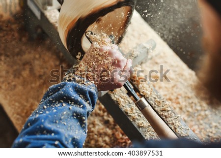 Worker's hands in  blue jeans suit working with woodcarving machine, instruments and wood, shavings on table, close up, woodworking, copy space.