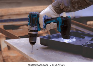 A worker's hands drill plywood with a battery-powered electric drill, close-up...