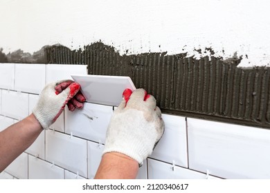 Workers Hands Installing Glazed Ceramic Tiles On The Kitchen Wall. A Handyman Using A Tile Spacer To Adjust The Tile Level. Repair Work, Construction Details