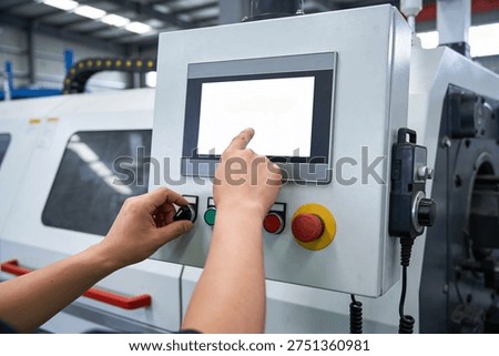 A worker's hands interact with a digital interface and physical buttons on a complex manufacturing equipment control system