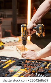 Worker's hands on a workbench with different tools drill a wooden part using a cordless drilldriver