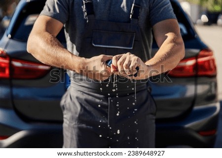 Worker's hands squeezing a wet rag at car wash station.