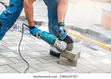A worker's hands work with an angle grinder during sawing the concrete block.