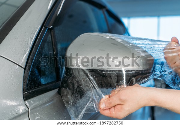 Workers hands wraps\
wet Paint Protection Film or anti-gravel protection coating on car\
mirror. Car detailing
