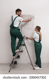 Workers Hanging Stylish Wall Paper Sheet Indoors