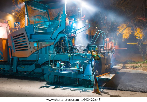 Workers with heavy machinery repairing asphalt road\
at night time