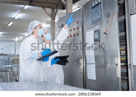 Workers inspecting control panel in factory, Quality control inspectors monitoring industrial machine control panel in a factory, Technicians checking electronic equipment in a food processing plant