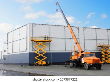 Workers Install Big Billboard On The Unfinished Building Supermarket. Construction Crane. 