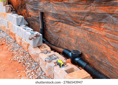 Workers install drainage system with blocks, pipes in yard during works retaining wall