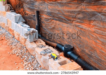 Workers install drainage system with blocks, pipes in yard during works retaining wall