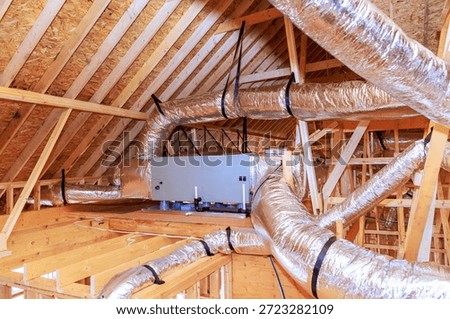 Workers install ducting ventilation systems in attic space of house under construction.