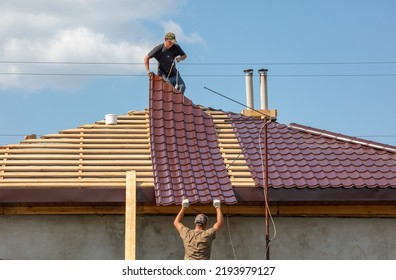 Workers install metal roofing on the wooden roof of a house. Technology - Shutterstock ID 2193979127
