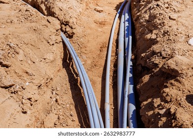 Workers install various electrical pipes in deep trench at construction site