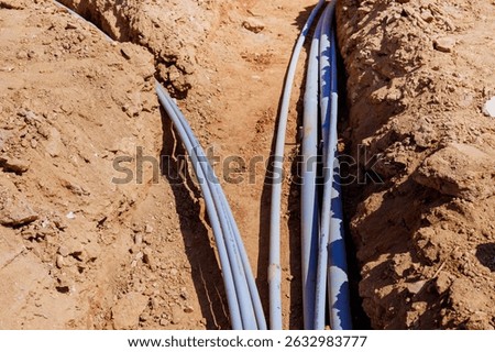 Workers install various electrical pipes in deep trench at construction site