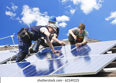 Workers Installing Alternative Energy Photovoltaic Solar Panels On Roof