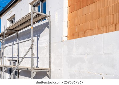 Workers installing external thermal insulation with scaffolding on residential building