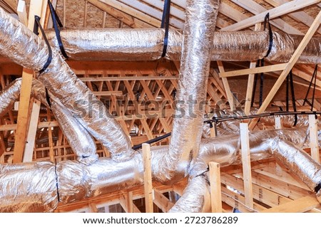Workers are installing metal ductwork in attic of construction site, wooden beams support structure.