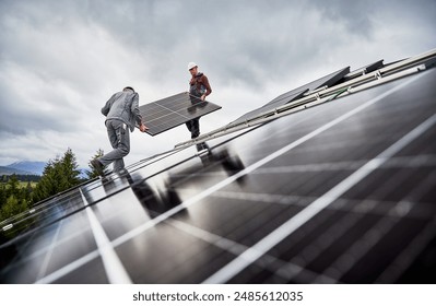 Workers installing solar battery on a roof of house. Male engineers carrying PV panel. Concept of green energetic resources.