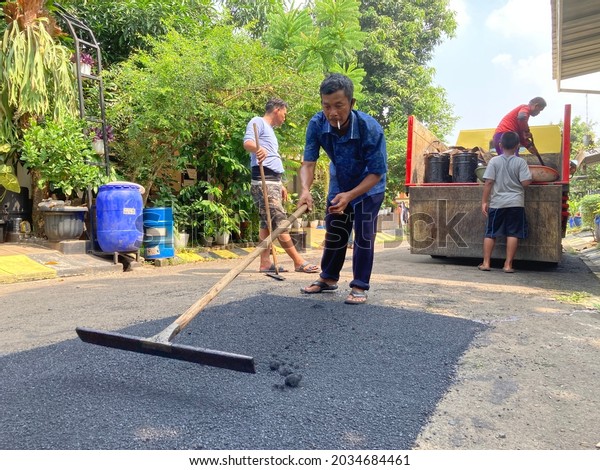 Workers level hot new asphalt before it is
compacted with the vibration of a heavy roller on a residential
road in Bogor, Indonesia. June 1, 2021. Heavy Vibration Roller on
asphalt pavement is
working