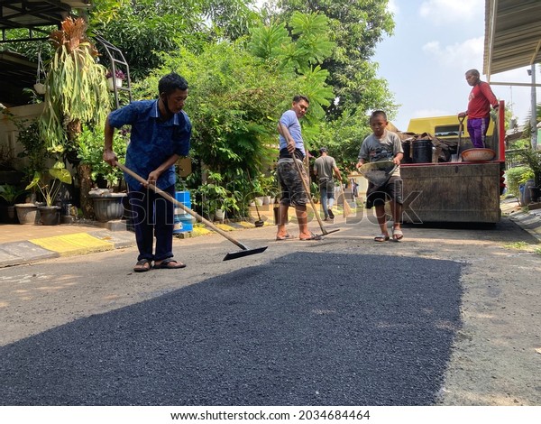 Workers level hot new asphalt before it is
compacted with the vibration of a heavy roller on a residential
road in Bogor, Indonesia. June 1, 2021. Heavy Vibration Roller on
asphalt pavement is
working