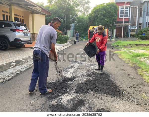 Workers level hot new asphalt before it is\
compacted with the vibration of a heavy roller on a residential\
road in Bogor, Indonesia. June 1, 2021. Heavy Vibration Roller on\
asphalt pavement is\
working