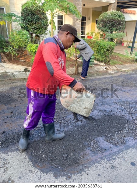 Workers level hot new asphalt before it is\
compacted with the vibration of a heavy roller on a residential\
road in Bogor, Indonesia. June 1, 2021. Heavy Vibration Roller on\
asphalt pavement is\
working