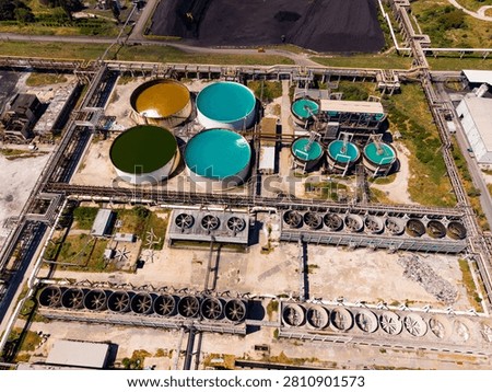 Workers manage operations at a processing facility featuring various large tanks filled with different colored liquids. The scene shows extensive machinery and piping.