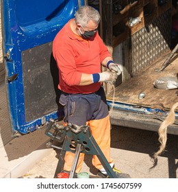 Workers With Masks During The Lockdawn For The Covid-19 Pandemic, With A Pipe Cutter, Cut A Galvanized Steel Pipe Positioned On A Stand To Perform A Repair Of An Underground Gas Line.