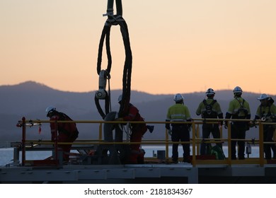 Workers On Dockyard Next To Lifting Shackle, Cables And Hook Lifting Device 