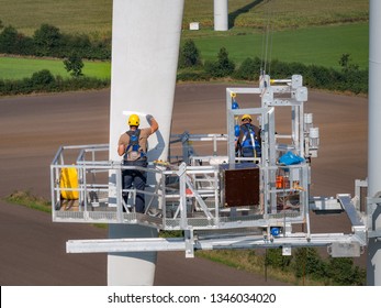 Workers On A Hanging Platform Repair A Damaged Rotor Blade On A Wind Turbine