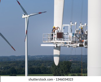 Workers On A Hanging Platform Repair A Damaged Rotor Blade On A Wind Turbine