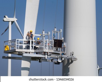 Workers On A Hanging Platform Repair A Damaged Rotor Blade On A Wind Turbine