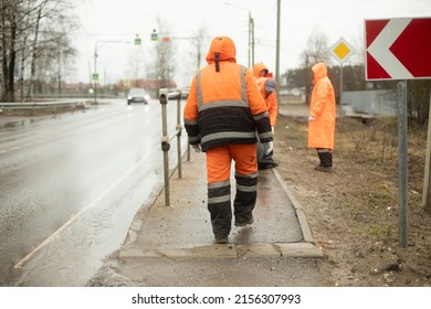 Workers On Road. Road Workers Clean Up Garbage. People In Orange Clothes. Transport Service Maintains Side Of Highway.