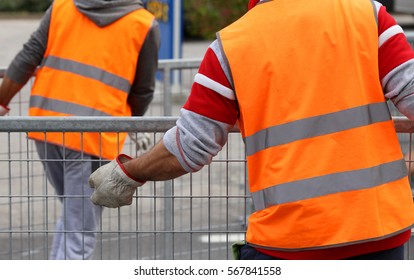 workers with orange high-visibility vest while moving the iron fences to delimit the space reserved for spectators during the event