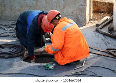 Workers Over The Open Sewer Hatch On A Street. Concept Of Repair Of Sewage, Underground Utilities, Water Supply System, Cable Laying, Water Pipe Accident