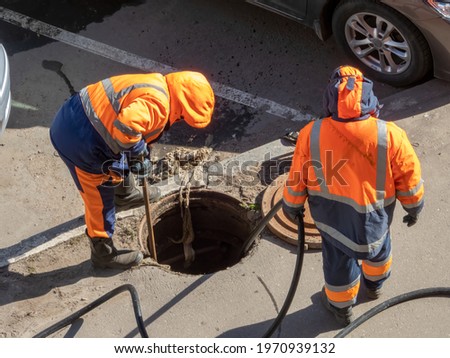 Workers over the open sewer hatch on a street. Repair of sewage, underground utilities, water supply system, water pipe accident