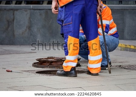 Workers over the open sewer hatch on a street. Concept of repair of sewage, underground utilities, water supply system, cable laying, water pipe accident