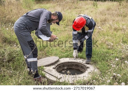 Workers in overalls peer into an open manhole, inspecting faulty water pipes and water meters.