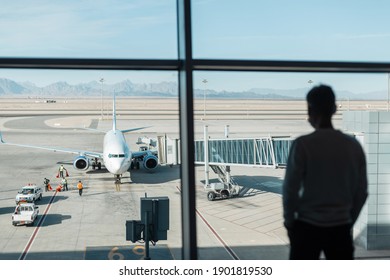 Workers Personnel Serve And Prepare The Aircraft For The Flight At The Airport. Man Is Waiting For Boarding. Business Guy Silhouette Near The Window Looks At The Plane Before Takeoff