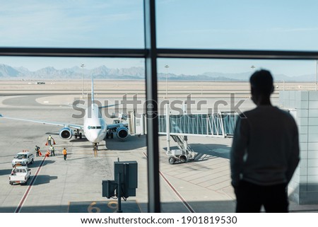 Workers personnel serve and prepare the aircraft for the flight at the airport. Man is waiting for boarding. Business guy silhouette near the window looks at the plane before takeoff