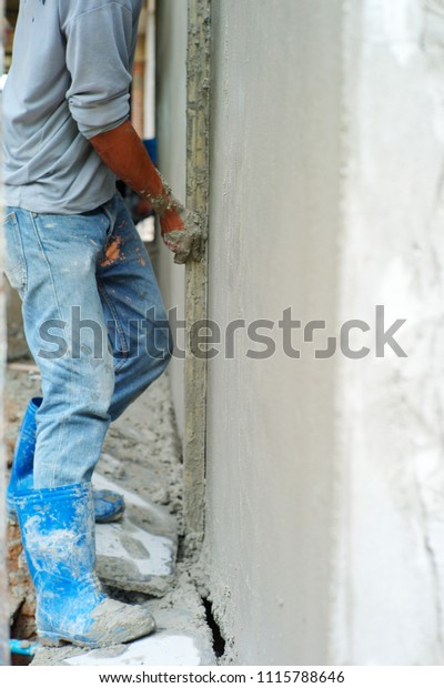 Workers plastering the concrete wall with\
trowel at the house under construction.\
