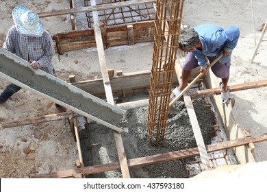 Workers pour ready mix concrete from mix concrete vehicle to a footing of a column, reinforcement with steel. Lay on ground above plastic cover sheet. With square formwork.  