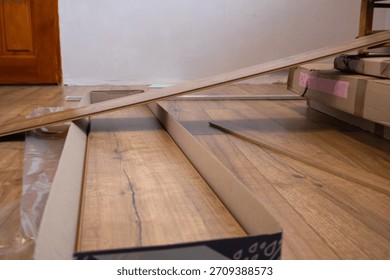 Workers are preparing to install laminate flooring in a room, with planks and packaging visible on the floor